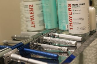 A collection of everyday skincare tools arranged aesthetically on a bathroom countertop, including a jade roller, facial brush, and serum bottles.