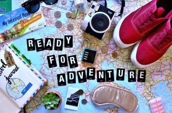 A collection of travel comfort items including a neck pillow, eye mask, and portable blanket arranged on a suitcase.